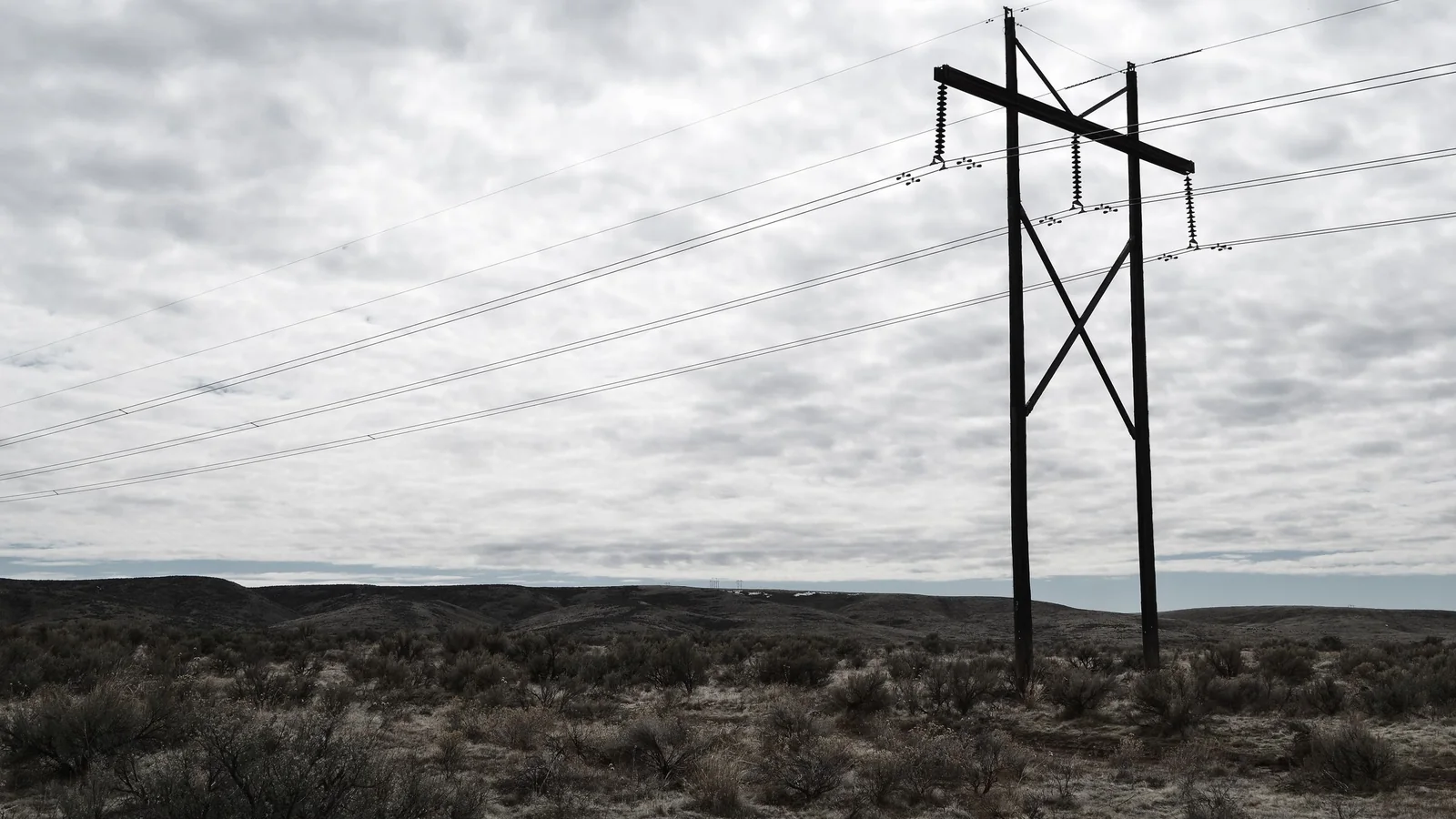 High-voltage transmission towers and power lines crossing open country under a cloudy sky