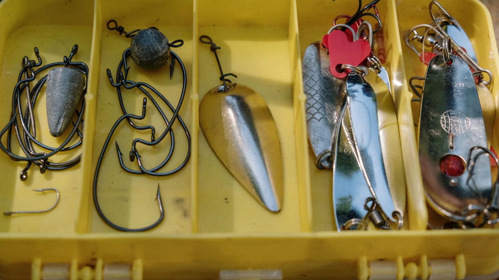 Yellow tackle box with compartments holding fishing hooks, spoons and lures