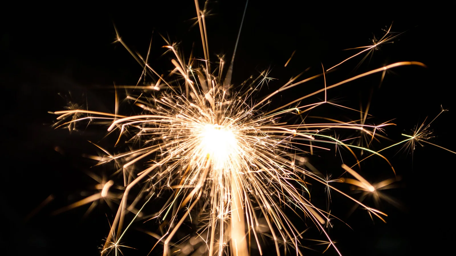 A burning sparkler throwing bright sparks against a black background