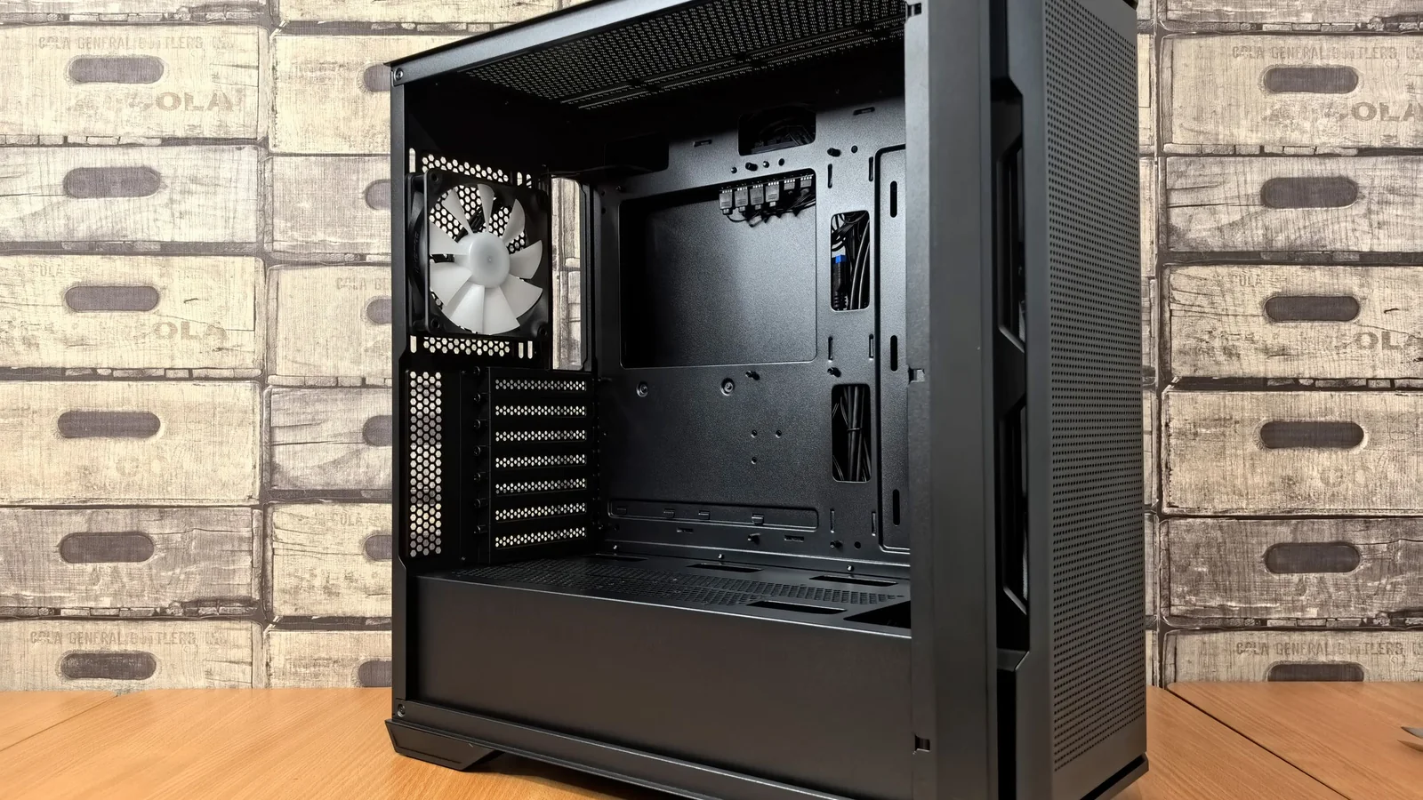 An open black PC tower case with a cooling fan, standing on a desk
