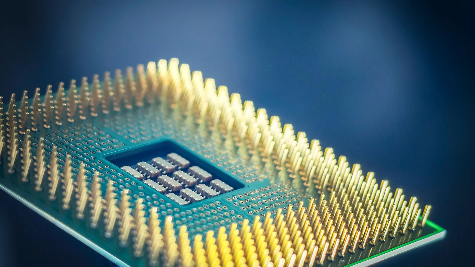 Close-up of a computer processor chip with rows of gold pins and a cluster of tiny components on a dark blue background